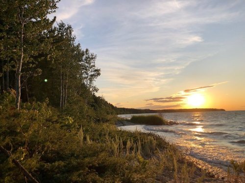 Sunset over a tranquil lake, with trees lining the shore and gentle waves reflecting the golden light.