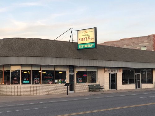 Exterior of The Original Kenny's Restaurant, featuring a sign and large windows, with a bench outside.