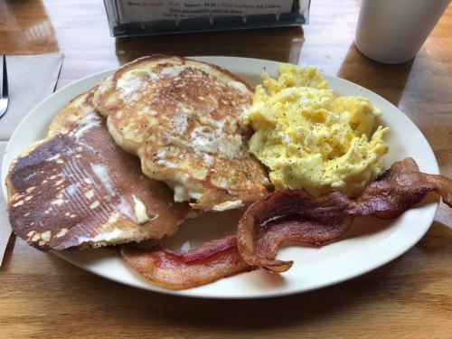 A plate of breakfast featuring pancakes, scrambled eggs, and crispy bacon.