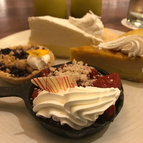 A plate with various desserts: cheesecake, pumpkin pie, and a mini tart topped with whipped cream and fruit.