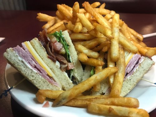 A plate with a sandwich layered with ham, cheese, lettuce, and bacon, surrounded by a pile of golden French fries.
