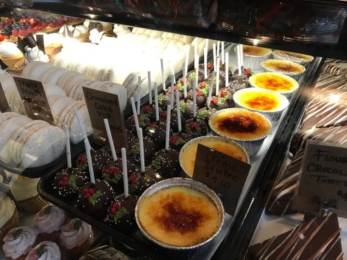 A display of assorted desserts, including crème brûlée, chocolate-covered treats, and macarons, in a bakery case.
