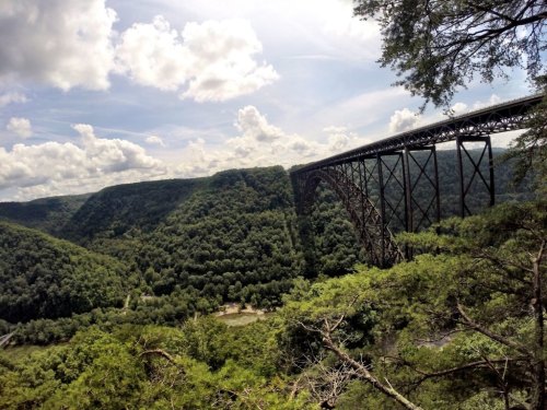 A large metal bridge spans a lush green valley under a partly cloudy sky.