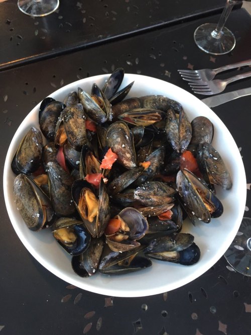 A white bowl filled with cooked mussels and diced tomatoes on a black table.