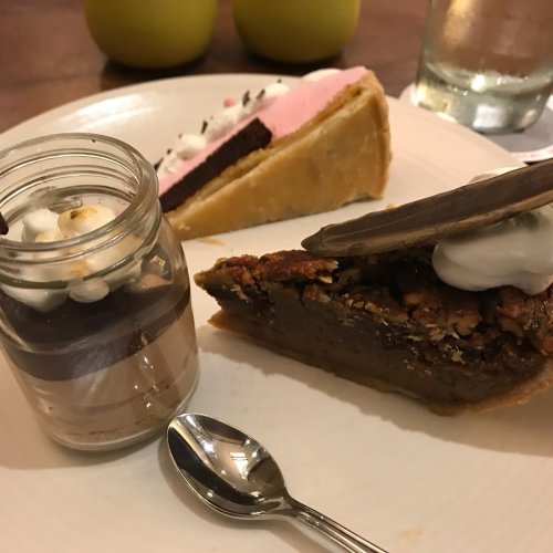 A plate with three desserts: a chocolate cake slice, a pie slice topped with cream, and a layered dessert in a jar.
