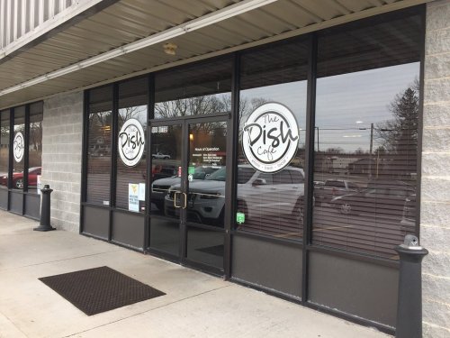 Exterior view of The Dish Café, featuring large windows and a sign, with parked cars visible outside.
