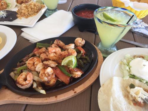 A sizzling platter of shrimp with vegetables, accompanied by a margarita and a side of salad and tortilla.