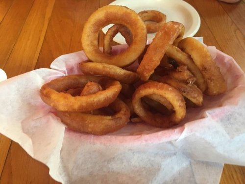 A basket of golden-brown onion rings on a bed of white paper, resting on a wooden table.