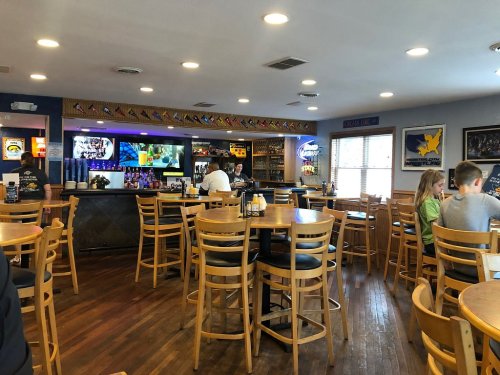 A cozy restaurant interior with wooden tables, a bar area, and patrons enjoying their meals. Brightly lit and welcoming.