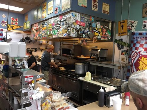 A busy kitchen with chefs cooking, surrounded by colorful vintage signs and stickers on the walls.