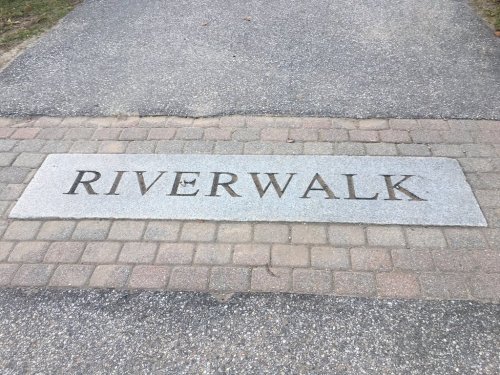 A stone pathway marker engraved with the word "RIVERWALK" on a paved surface.