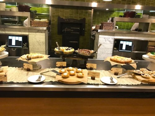 A dessert display featuring various pastries and cakes on a buffet table with labels and utensils.