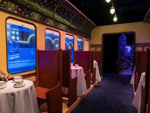 Interior of a train car with tables set for tea, featuring large windows and a cozy, festive atmosphere.