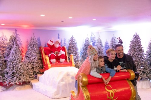A family poses in a festive setting with Santa Claus in a sleigh surrounded by snowy trees.