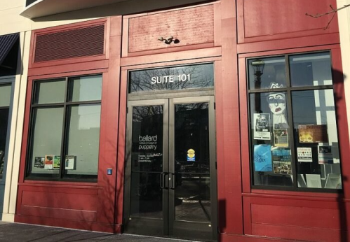 Red storefront with large glass windows and a door labeled "Suite 101," featuring various posters and signage.