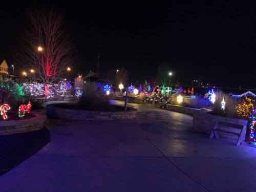 A pathway illuminated by colorful holiday lights, surrounded by festive decorations and trees at night.