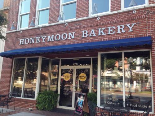 Exterior of Honeymoon Bakery, featuring a brick facade, large windows, and a blue awning with outdoor seating.