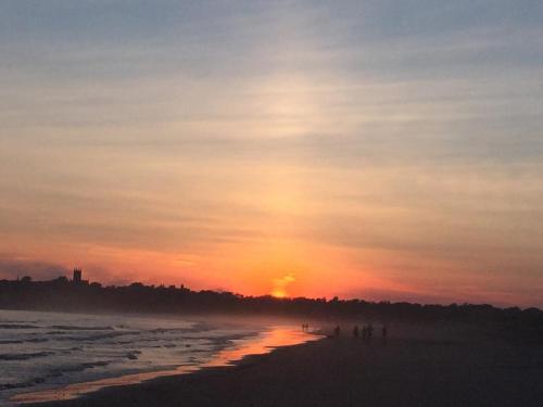 A serene beach at sunset, with soft waves and silhouettes of people walking along the shore against a colorful sky.