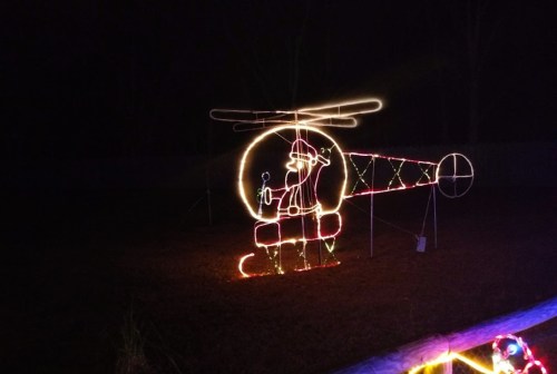 A festive light display of a helicopter with Santa holding a gift, set against a dark night sky.