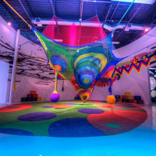 Colorful indoor play area featuring a large, vibrant net structure hanging from the ceiling over a patterned floor.