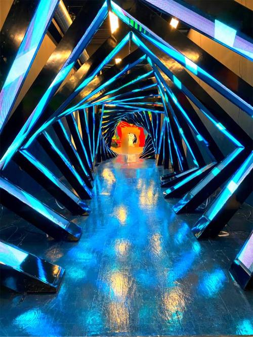 A futuristic hallway with blue-lit, angular structures creating a tunnel effect, leading to a bright red entrance.