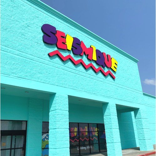 Bright turquoise building with colorful "SEISMIQUE" sign and wavy design on the facade under a clear blue sky.