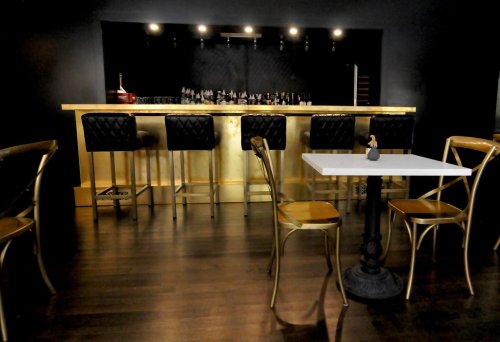 A stylish bar with a gold counter, black stools, and a small table in a modern, dimly lit setting.