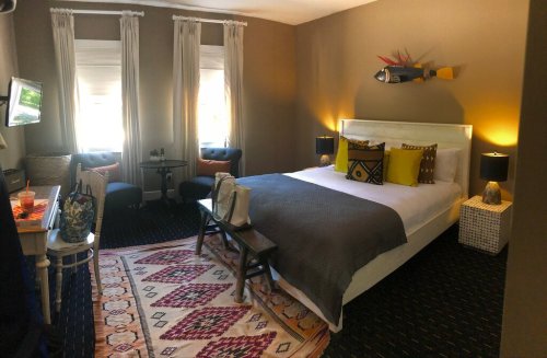 Cozy hotel room with a large bed, decorative pillows, a rug, and two windows letting in natural light.