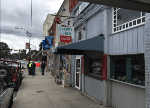 A street view of Snappy Lunch, featuring a retro sign and nearby pedestrians in a small town setting.