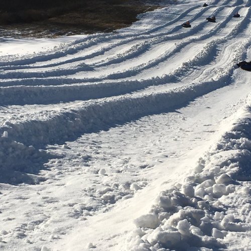 A snowy slope with ridges and tracks, where people are sledding down on tubes.