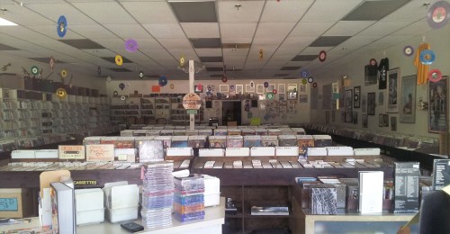 A vintage music store filled with vinyl records, cassettes, and CDs, decorated with colorful hanging records.