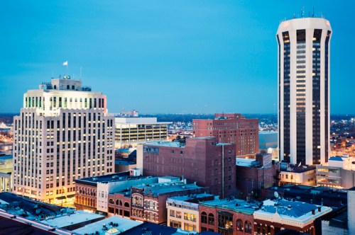City skyline at dusk featuring modern skyscrapers and historic buildings, illuminated against a twilight sky.
