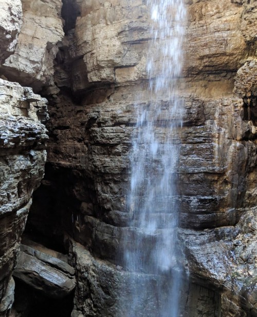 A waterfall cascading down rocky cliffs in a narrow canyon, surrounded by textured stone walls.