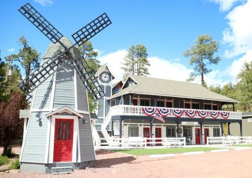 A charming building with a windmill, decorated with red, white, and blue bunting, surrounded by trees and blue skies.