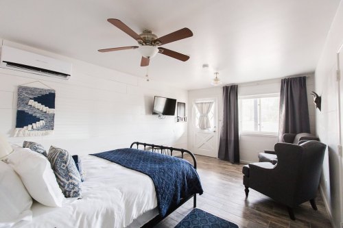 Cozy bedroom with a bed, armchair, TV, and large window, featuring light walls and wooden flooring.
