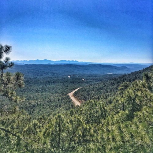 A panoramic view of lush green mountains and a winding road under a clear blue sky.