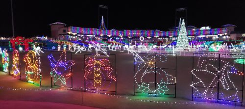 Colorful holiday lights decorate a park, featuring trees and festive designs against a night sky.