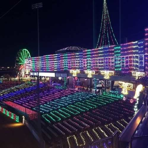 A brightly lit stadium decorated with colorful lights, featuring a tall Christmas tree and a Ferris wheel in the background.