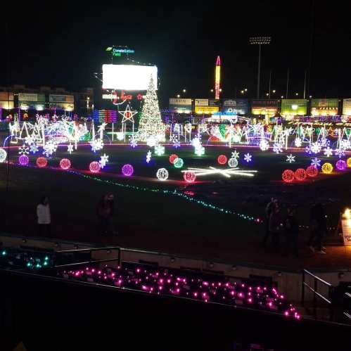A festive display of colorful Christmas lights illuminating a park at night, featuring a decorated tree and various holiday shapes.