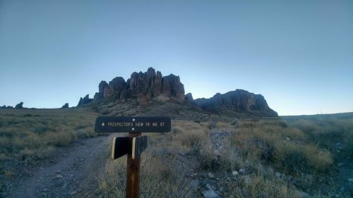 A trail sign for "Prospector's View Trail No. 57" with rocky mountains in the background under a clear sky.