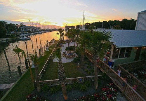 A scenic view of a marina at sunset, with palm trees, boats, and a landscaped area along the water.