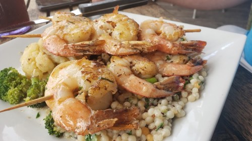 Grilled shrimp skewers served on a bed of couscous with broccoli and cauliflower.