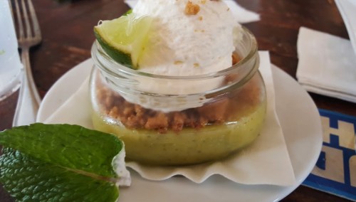 A dessert in a glass jar with lime, whipped cream, and a crumbly topping, garnished with a mint leaf.