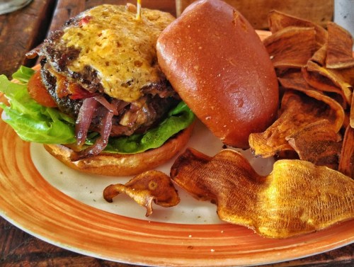A juicy burger with melted cheese, lettuce, and tomato, served with crispy sweet potato chips on the side.