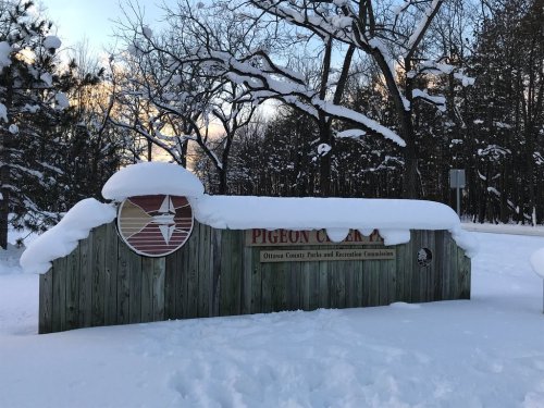 Sign for Pigeon County, covered in snow, surrounded by trees in a winter landscape.