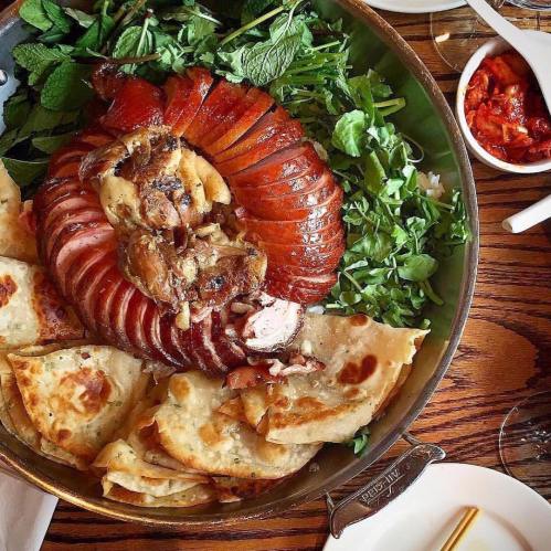 A large platter featuring roasted meat, flatbreads, fresh greens, and a side of kimchi.
