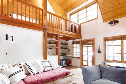 Cozy interior of a wooden cabin with high ceilings, a loft, and comfortable seating areas. Natural light fills the space.
