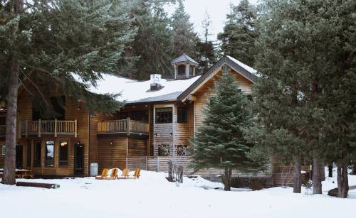 A cozy wooden cabin surrounded by snow-covered trees, with a porch and outdoor seating.