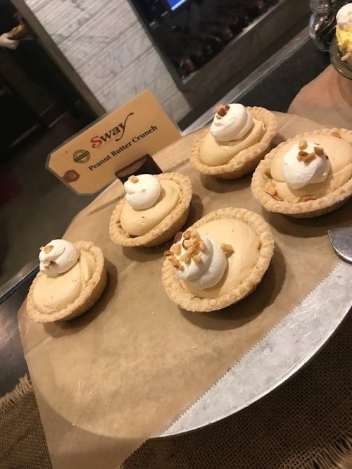 Five peanut butter crunch mini pies topped with whipped cream and crushed peanuts on a serving tray.