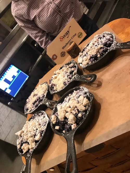 Five small cast iron skillets filled with blueberry crisp, topped with a crumbly topping, on a wooden surface.